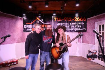 Three musicians posing on stage with guitars and microphones.
