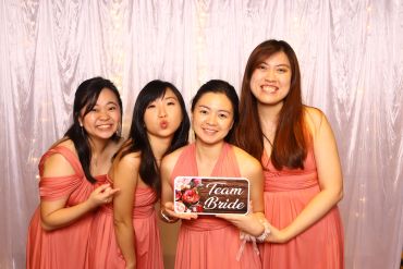 Four bridesmaids in matching coral dresses smiling and holding a 'Team Bride' sign.