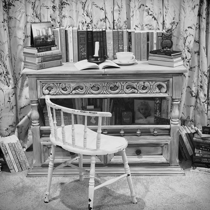 bookshelf/table top with books, coffee, old fashioned candle holder, captains chair, piles of books