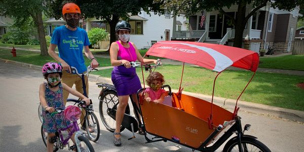 Woman, man, two children wearing masks and getting ready to ride bikes.