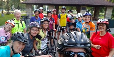 Group of smiling bicyclists standing in a park wearing bike helmets