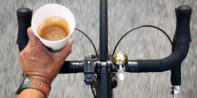 Looking down at the handlebars of a moving bike. One hand holds coffee.