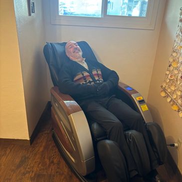 Elderly man relaxing in a massage chair near a window in a cozy room.
