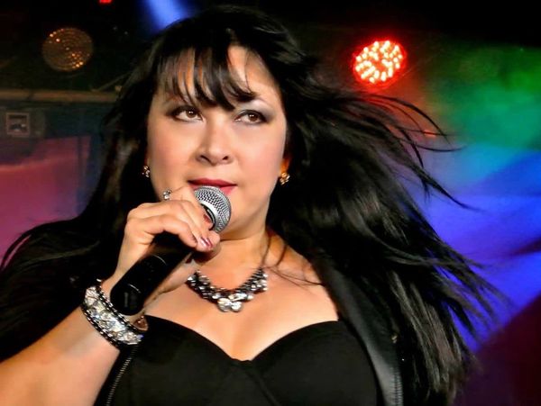 Female singer passionately performing on stage with colorful lights behind.