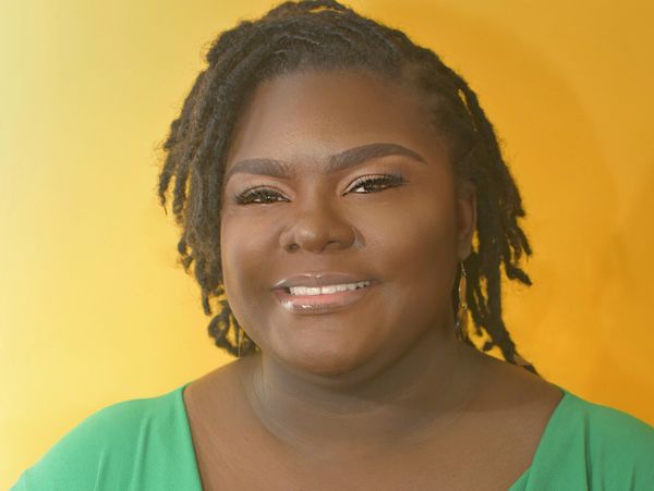 Smiling woman with dreadlocks against a yellow background.