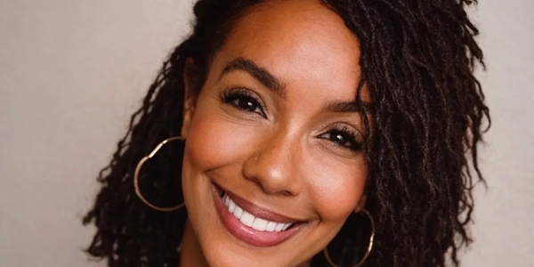Close-up of a smiling woman with curly hair and hoop earrings.