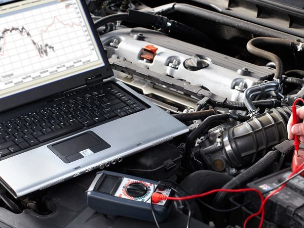 Laptop and multimeter diagnosing a car engine under the hood.