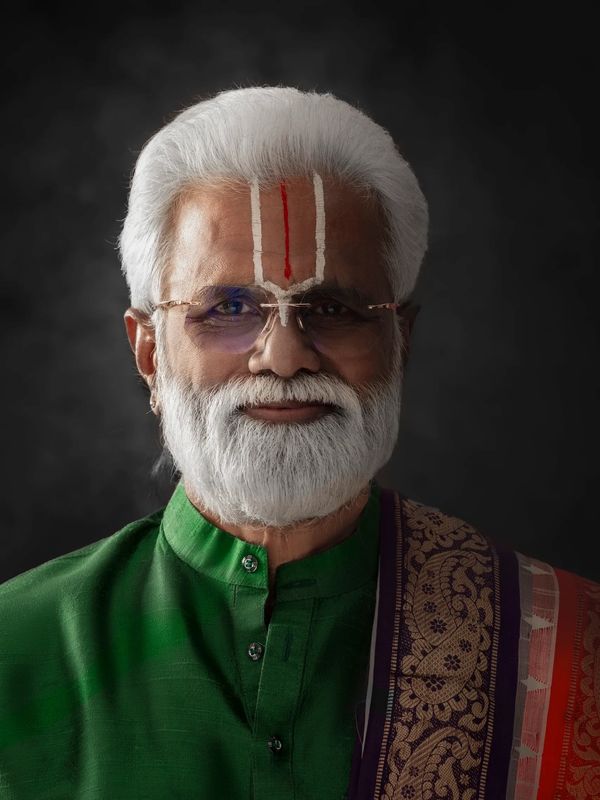 Elderly man with white beard in traditional attire and forehead markings.
