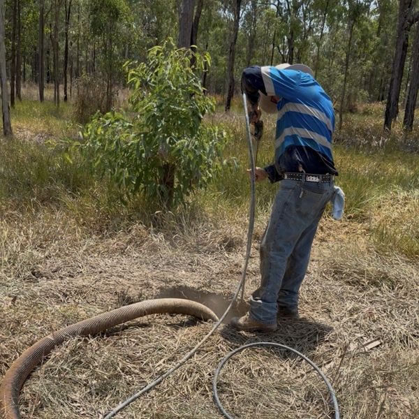 Man using a tool to clear or dig in a dry grassy field.