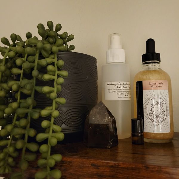 Decorative plant and wellness items including crystal, spray, and serum on wooden surface.