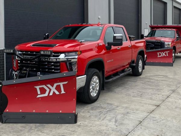 Two red trucks with large DXT snowplows attached.
