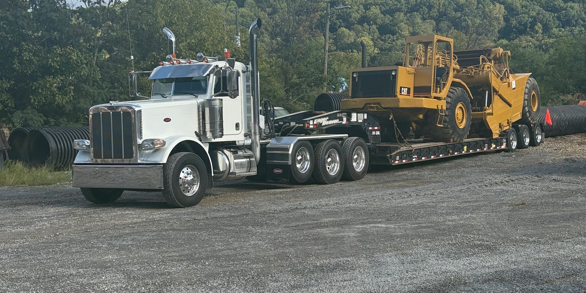 White truck hauling yellow construction equipment.