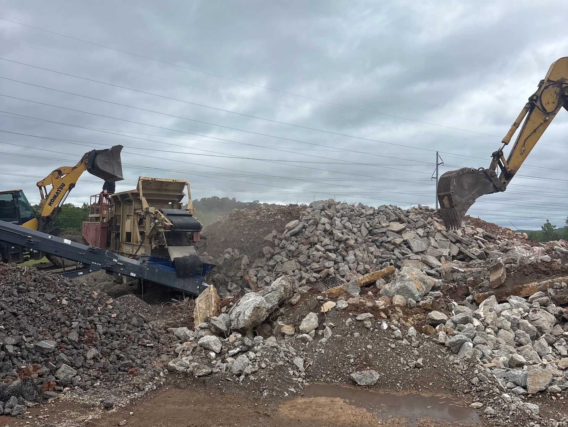 Construction site with machinery and rubble under cloudy sky.