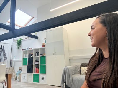 Woman smiling indoors in a bright room with shelves.