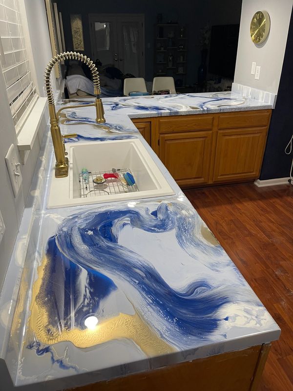 Kitchen countertop with blue, white, and gold marble-like design and brass faucet.