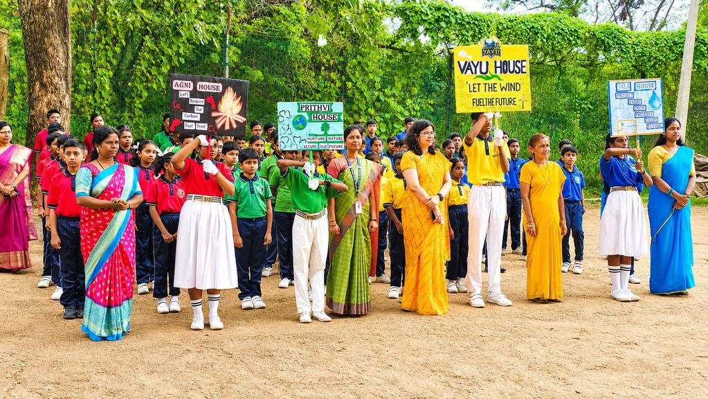 Students and teachers in colorful uniforms holding environmental awareness signs outdoors.