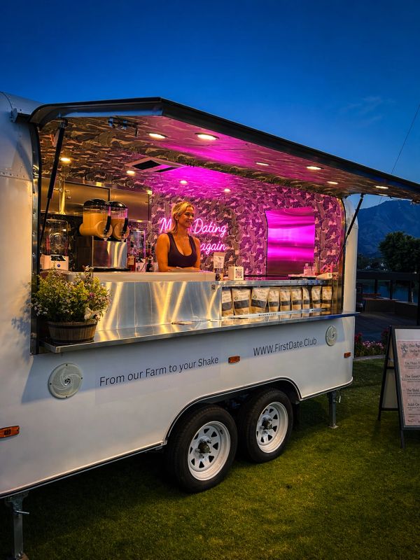 Woman serves shakes in a decorated food truck at dusk.