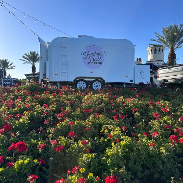 White trailer with "First Date Club" sign near flowers and palm trees.