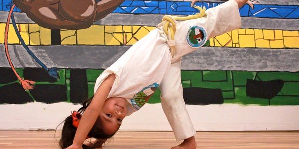 A child in a martial arts uniform doing a backbend indoors.