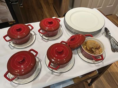 Red lidded pots with food on a table alongside plates and utensils.