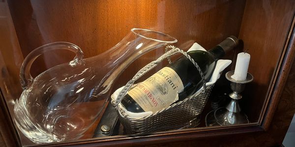 Vintage wine bottle and glass decanter displayed in wooden cabinet.