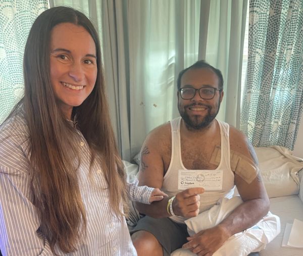 A man in a hospital bed with a woman smiling beside him.