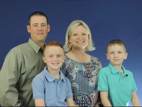 A family portrait with two adults and two boys smiling against a blue background.