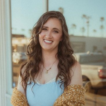 Young woman with long wavy hair smiling outdoors.