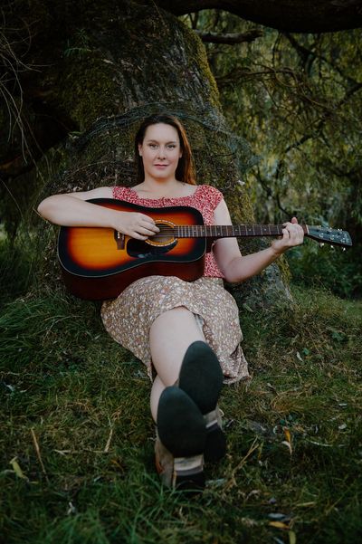 Woman sitting on grass playing an acoustic guitar.