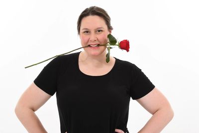 Woman smiling with a red rose in her mouth, wearing a black shirt.