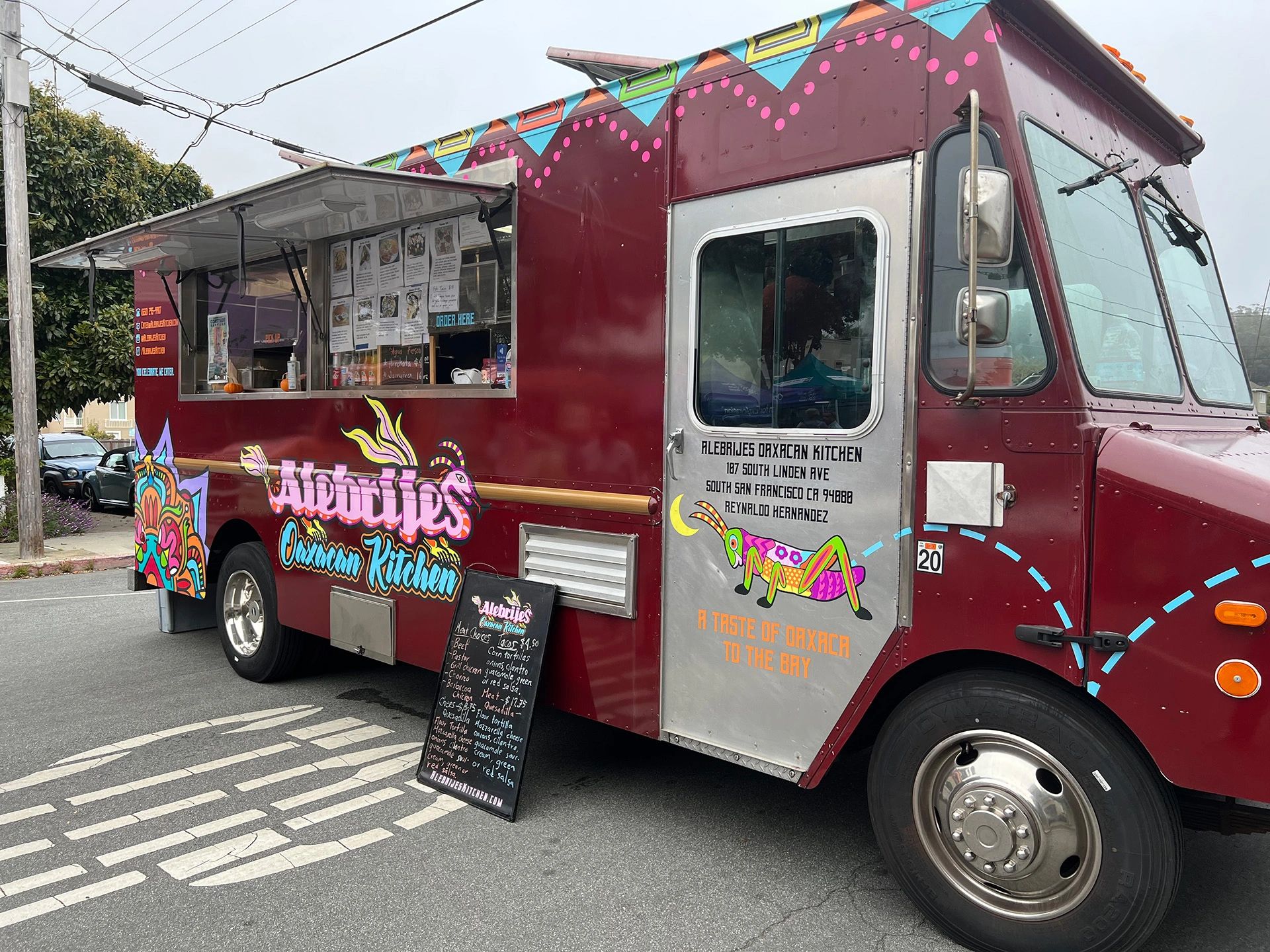 the alebrijes food truck. it is maroon with colorful oaxacan illustrations.