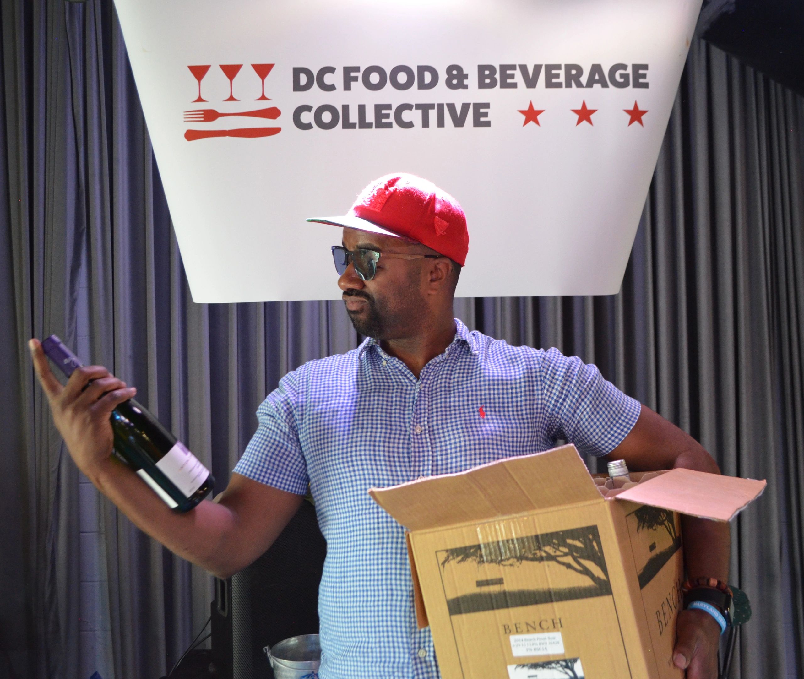 Man in red cap examining a wine bottle at DC Food &amp; Beverage Collective.