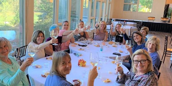 Group of women raising glasses in a celebratory toast around a table indoors.
