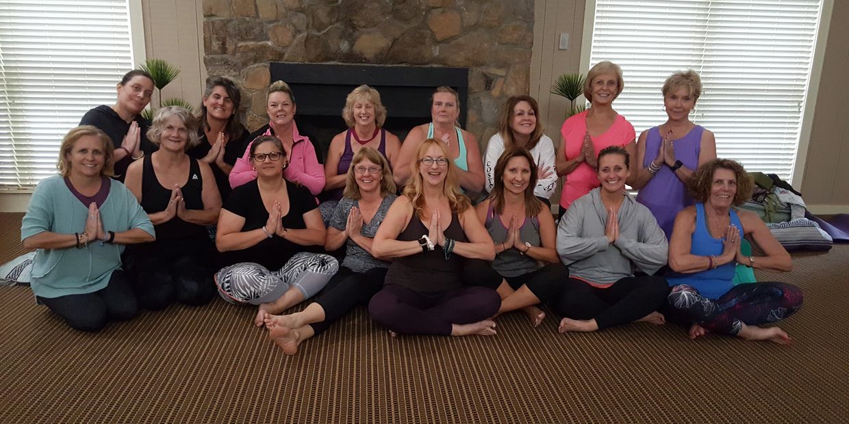 Group of women sitting in a yoga pose with hands in prayer gesture indoors.