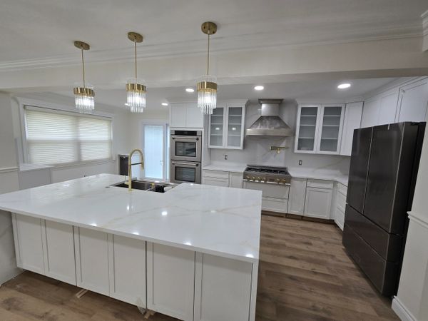 Modern kitchen with white cabinets, marble countertops, and gold fixtures.