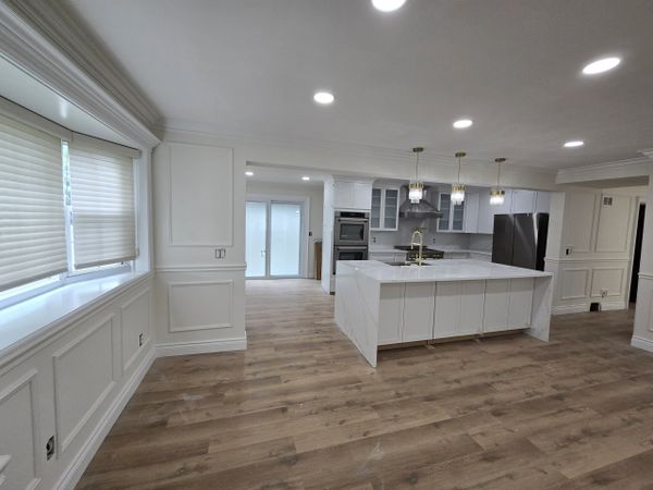 Modern white kitchen with large island and wood flooring.