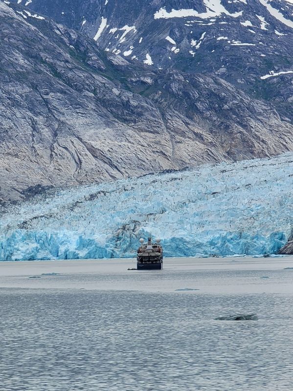Ship near a massive glacier in a mountainous fjord.