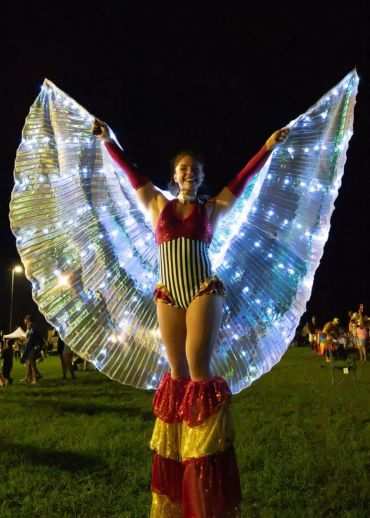 Performer in illuminated wings costume at night event.