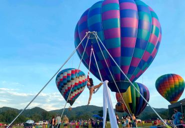 Aerial silk performer with hot air balloons at a festival.