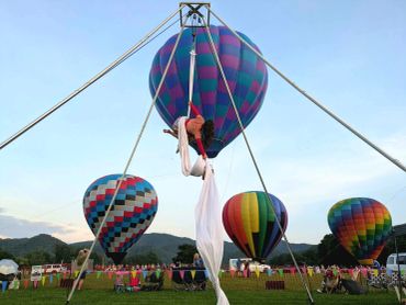 Woman performing aerial silk with hot air balloons in background.