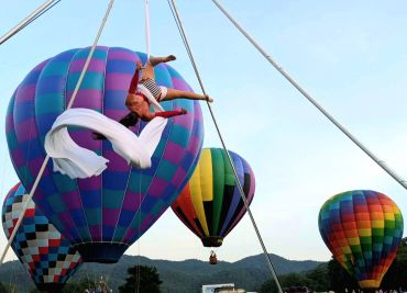 Aerial silk artist performs in front of hot air balloons.
