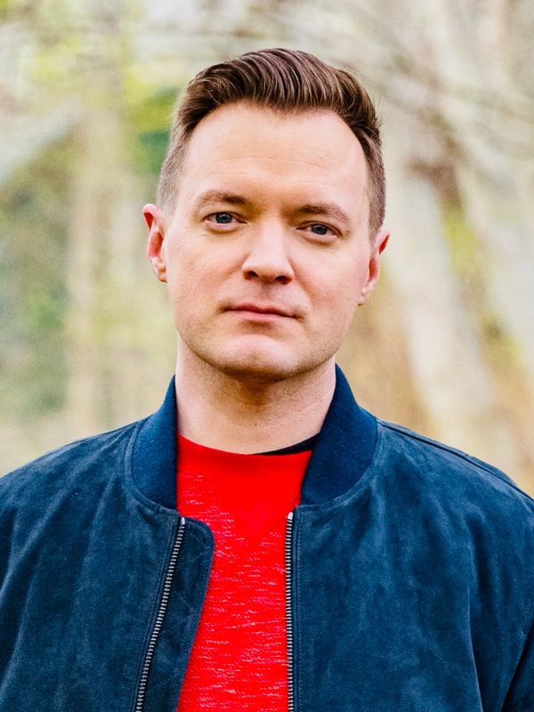 Portrait of a man wearing a blue jacket and red shirt outdoors.