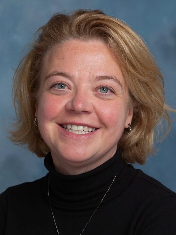 Smiling woman with blonde hair wearing a black turtleneck and silver necklace.
