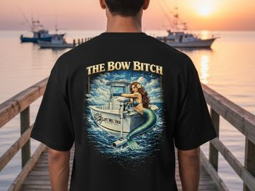 Person wearing a black shirt with a mermaid boat design at sunset on a dock.