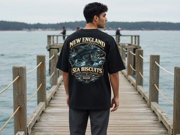 Man stands on a wooden pier wearing a black shirt with a fish graphic and 'New England Sea Biscuits' text.