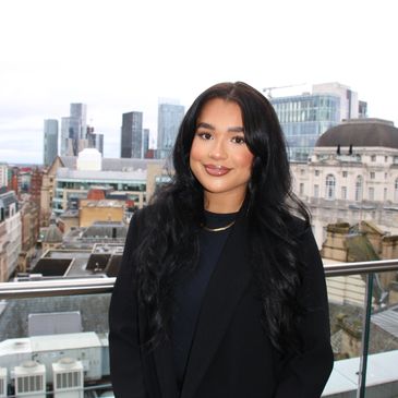 Young woman with long black hair posing on a rooftop with cityscape behind.