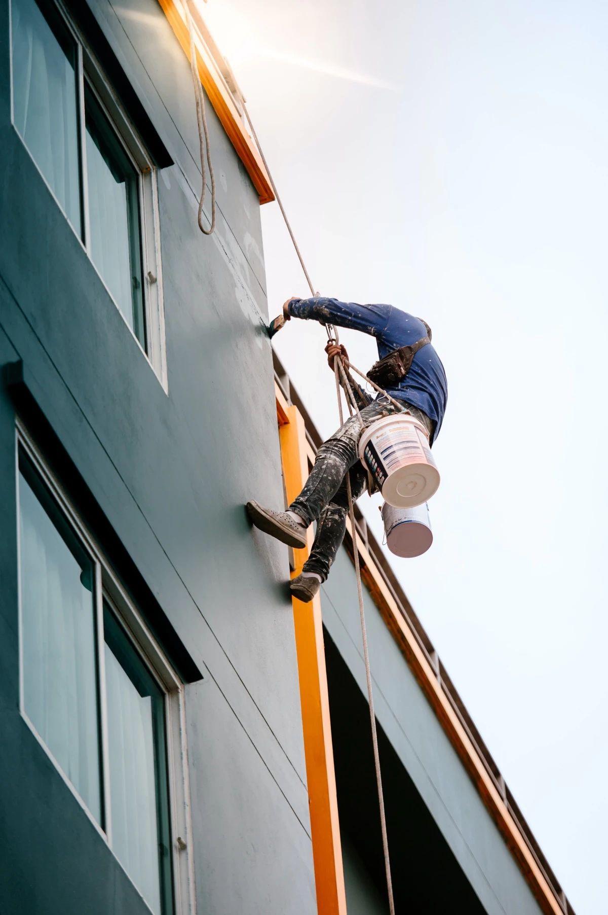 Painter absailing from the roof of a commercial building, painting as he goes. 