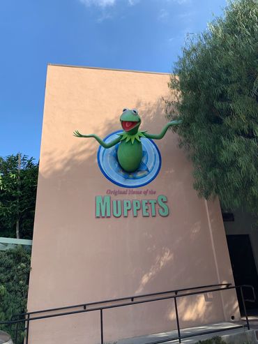 Kermit the Frog protruding from a wall with Muppets sign.