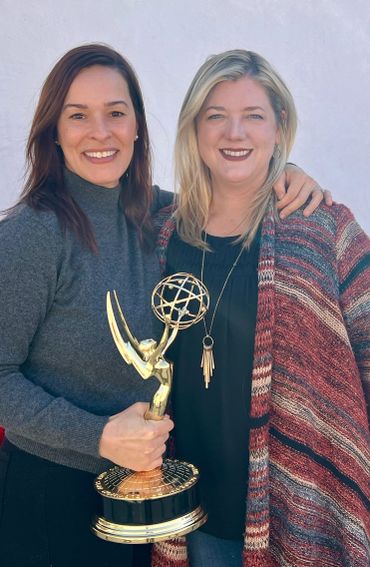 Two women smiling, holding an Emmy award together.