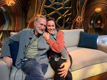 Two people smiling and sitting closely on a couch with a decorative background.